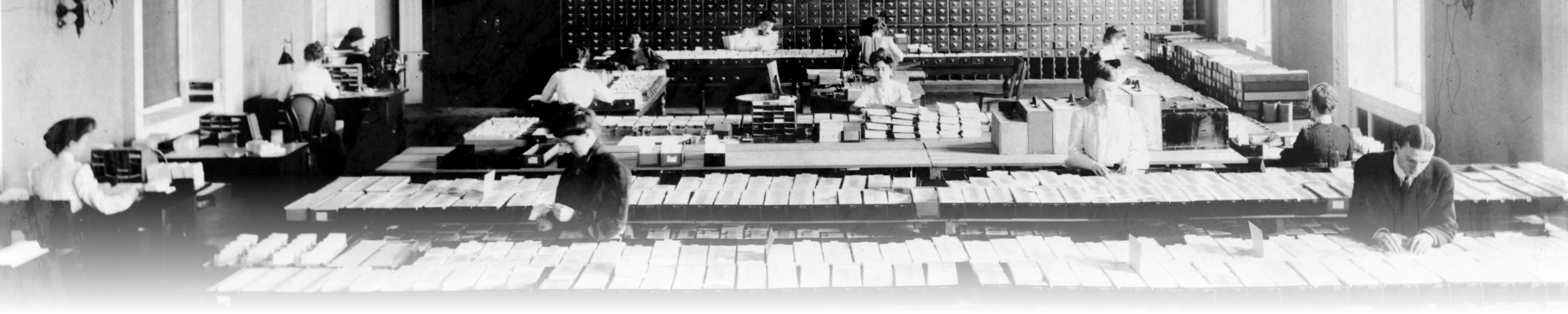A black-and-white historical photograph of the Library of Congress Card Division, showing clerks filing catalog cards across long tables in front of a wall of card-catalog drawer cabinets