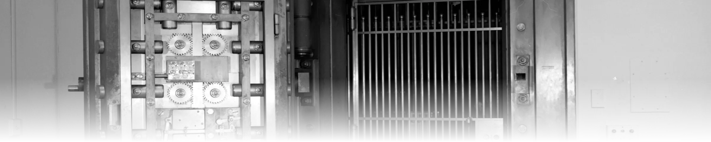 A 1914 Diebold bank vault door swung open, showing its inner locking mechanism of meshing drive gears and bolt-work beside a barred security gate