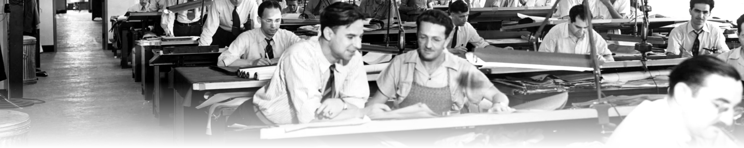 A black-and-white 1940s drafting room, rows of engineers at drafting tables with rolled blueprints on their desks