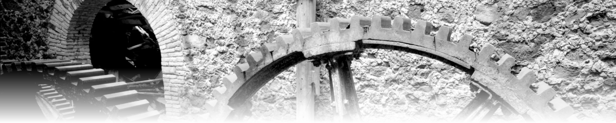 A black-and-white photograph of two interlocking cast-iron gears against a stone wall