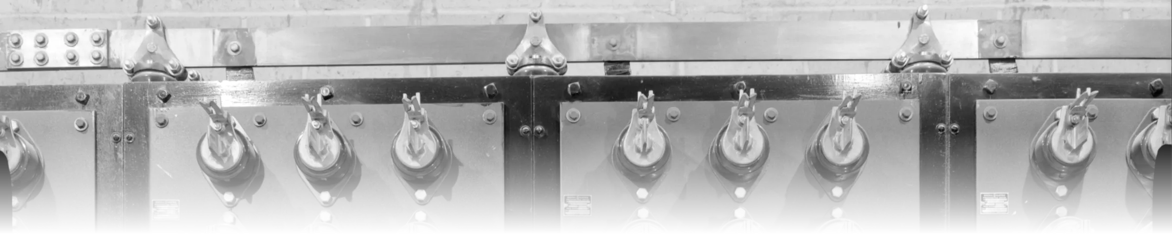A bank of three-phase knife switches on a 1930s-era industrial switchboard, each identical switch assembly mounted on its own labelled panel along a shared bus structure