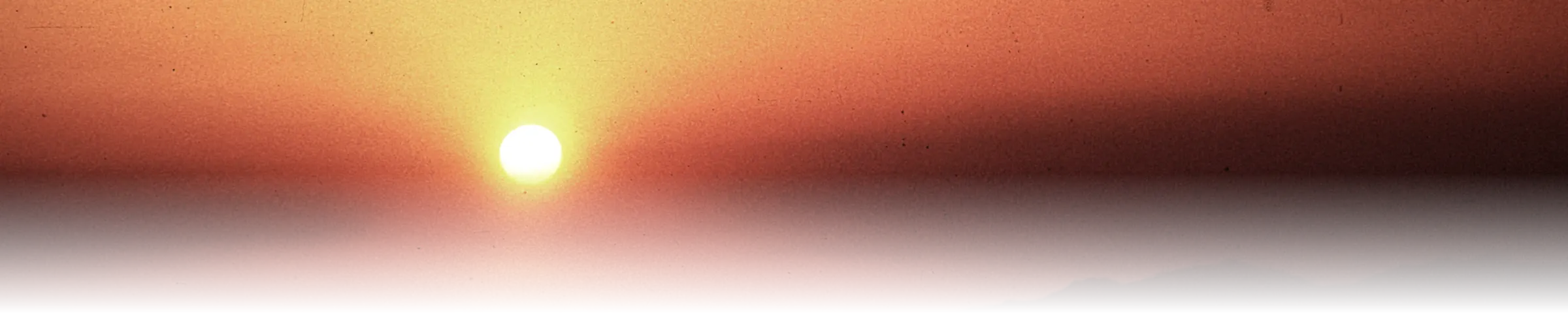 A hazy orange-red sunset gradating from pale gold through orange to deep red over a mountain ridge