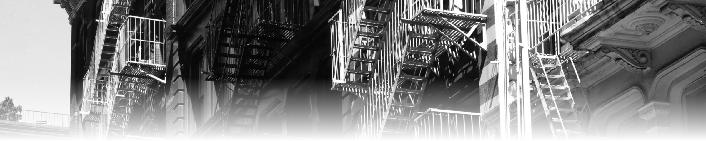 Zigzagging cast-iron fire escapes descending several adjoining building facades in SoHo, New York, each one a direct exit route bypassing the interior