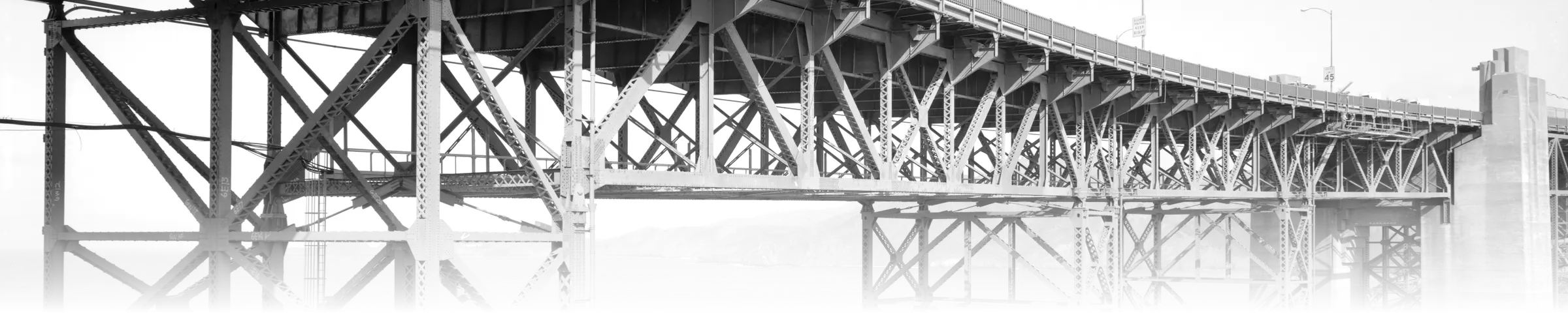 A black-and-white photograph of the Golden Gate Bridge steel truss structure and girders, viewed from below