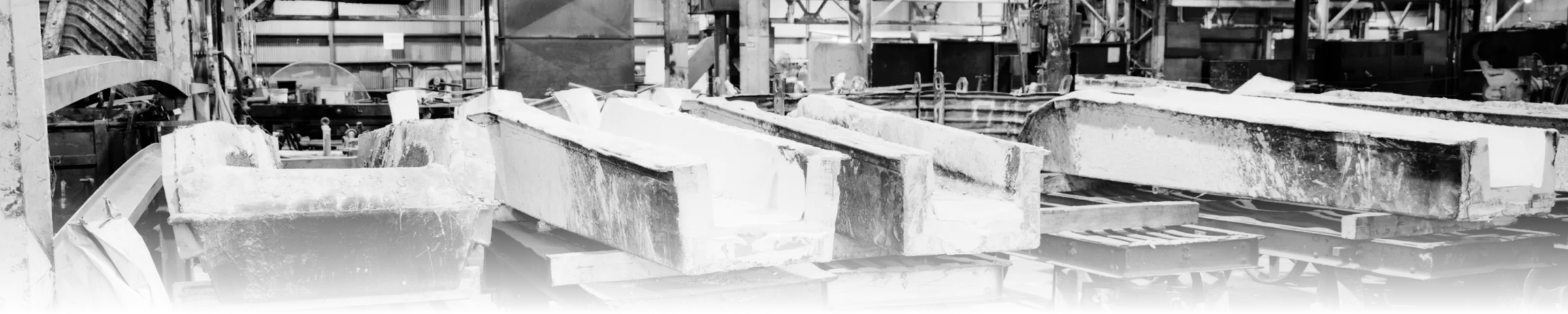 Refractory-lined runner-box moulds lined up on rail carts in a brass foundry casting shop, each cast to the same fixed shape