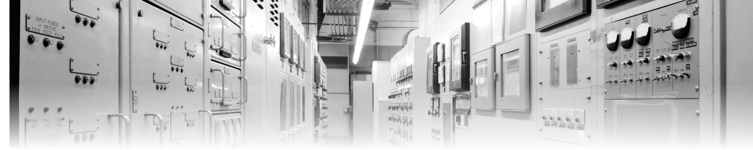 A wide, densely packed wall of labelled switch and instrument panels in a nuclear power station control room, each panel carrying its own named controls