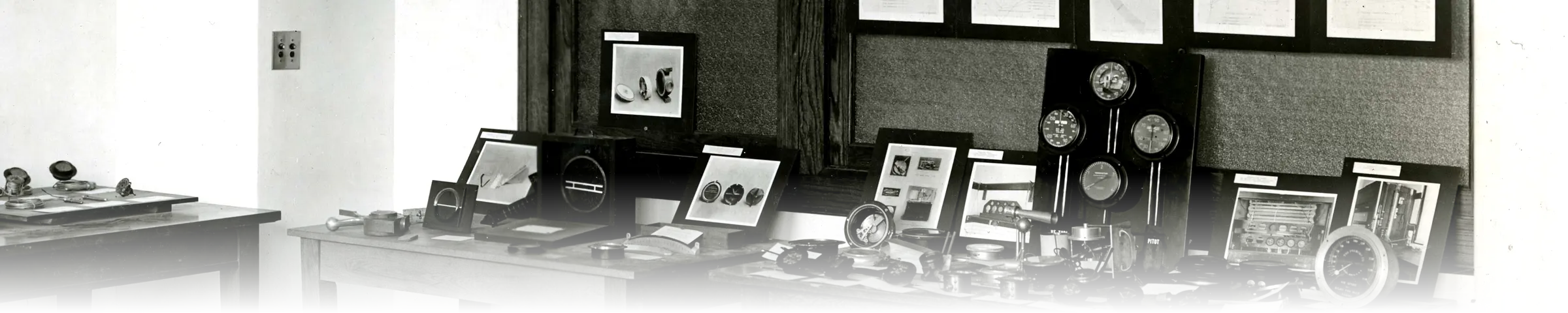 A black-and-white 1919 photograph of a standards-laboratory exhibit room, with tables and a labelled pegboard wall displaying categorised aeronautic measuring instruments and calibration charts