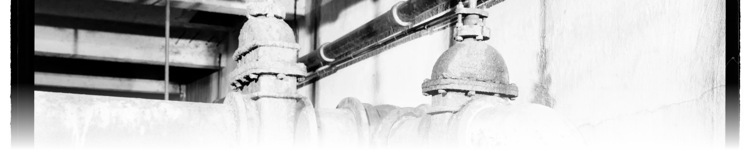 Historic black-and-white photograph of gate valves controlling sequential stages of a water filtration plant, main flood valve and crossover valve mounted side by side on the pipe run