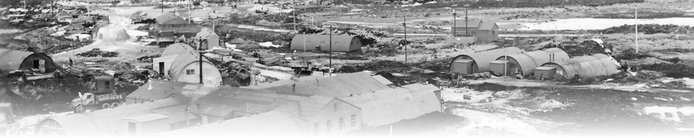 A black-and-white photograph of a WWII-era Quonset hut encampment, dozens of identical prefabricated arched-roof huts arranged across a snowy site