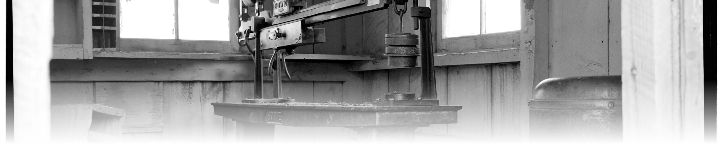 A Howe commercial platform scale inside a National Park Service-documented scale house, the branded beam and hanging counterweight surrounded by a ladder, barrel, and stove